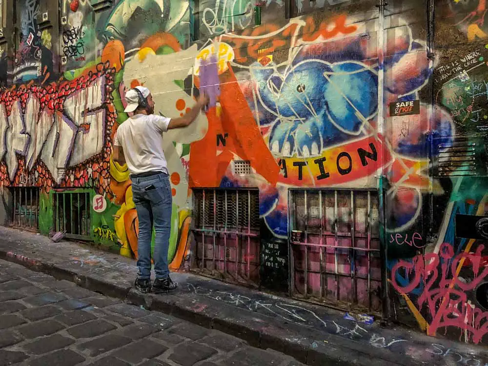 Graffiti Melbourne: Hosier Lane - man spray painting orange paint onto a wall